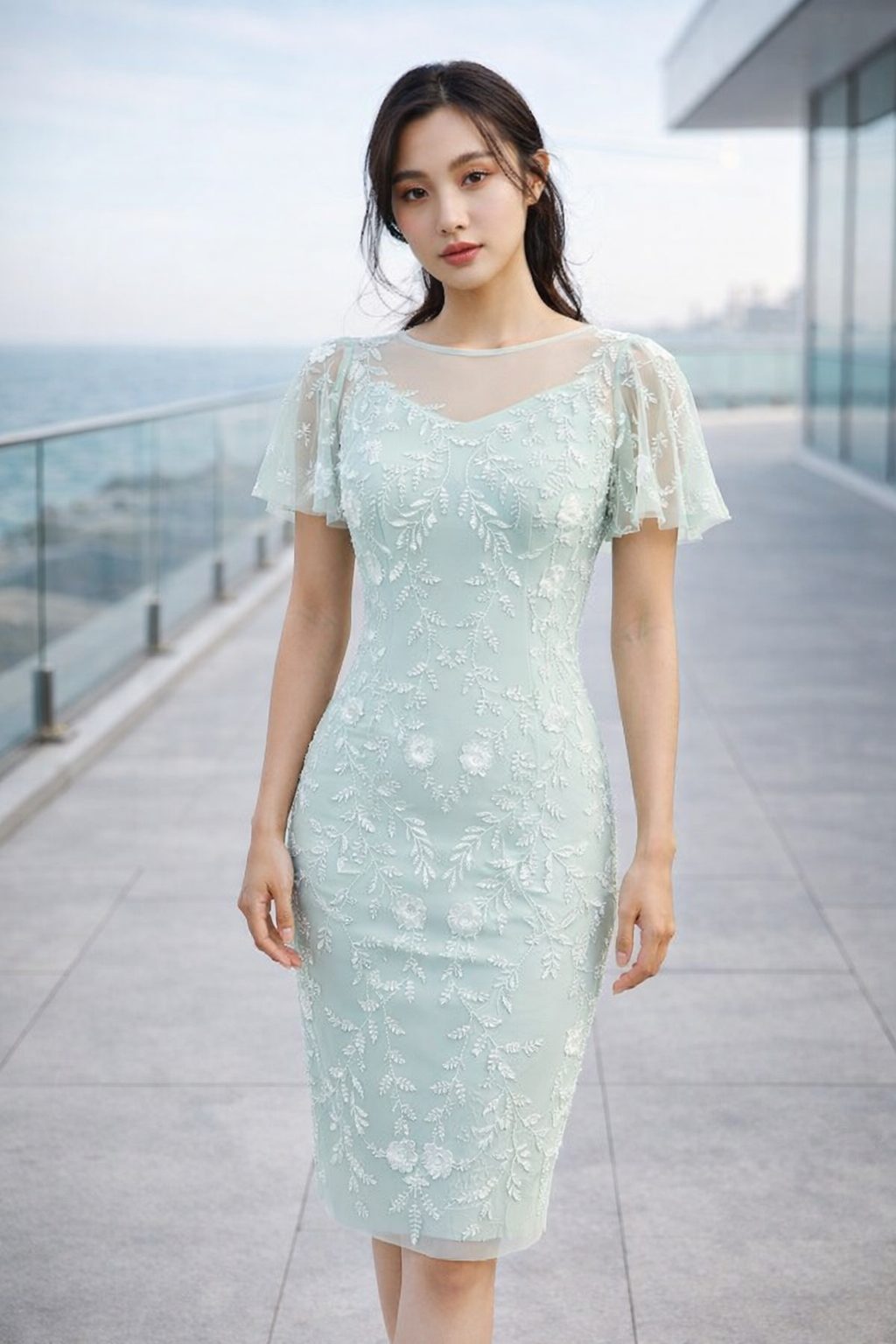 Woman wearing a mint green embroidered fitted midi dress with sheer flutter sleeves in a modern coastal editorial setting