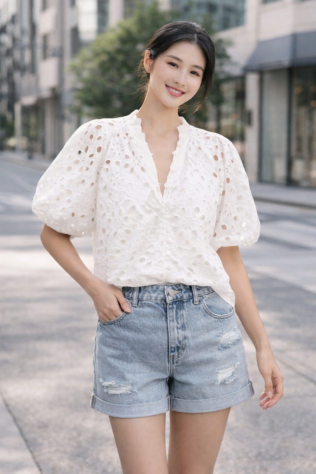 Woman wearing a white eyelet puff-sleeve blouse with light wash denim shorts in a modern outdoor street setting